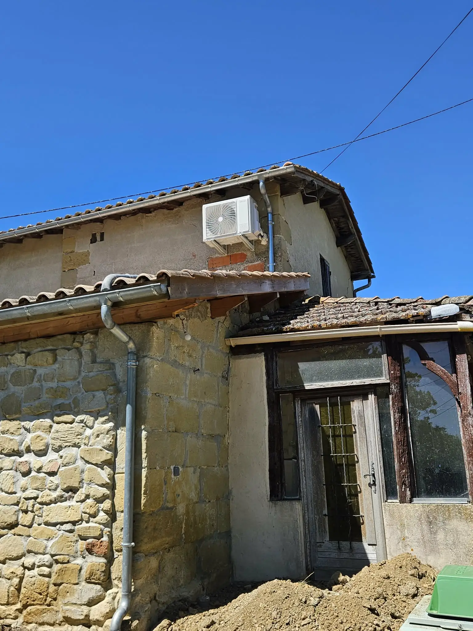 Unité extérieure de climatisation fixée en toiture sur une bâtisse en pierre