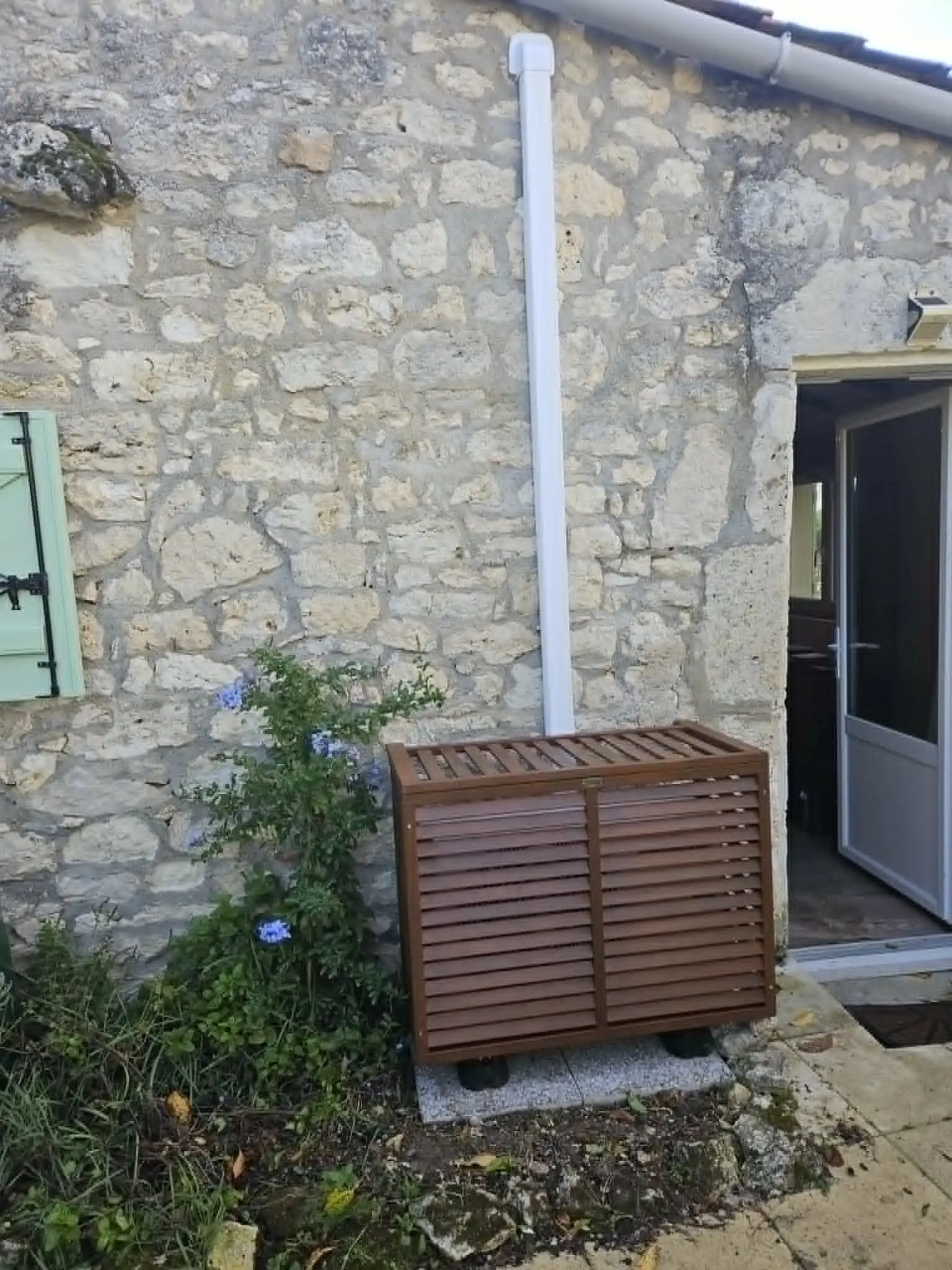 Unité extérieure protégée par un cache bois marron sur mur de pierre